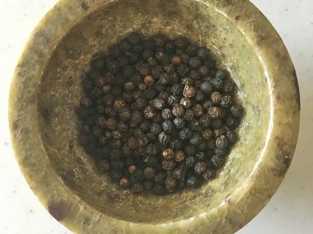 Whole black peppercorns in a brass bowl