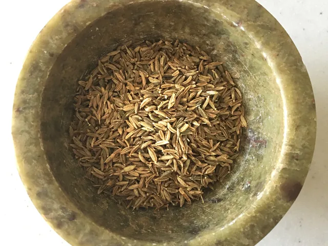 Elongated brown cumin seeds in a brass bowl
